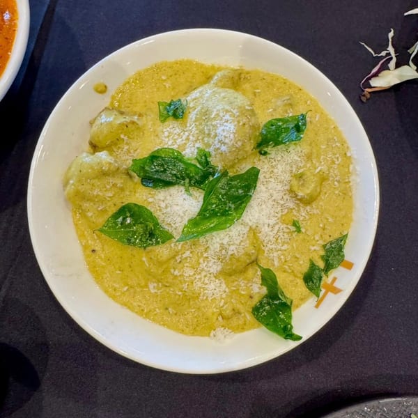 Indian dish with green dumplings in a creamy yellow sauce, garnished with fresh herbs and grated cheese.