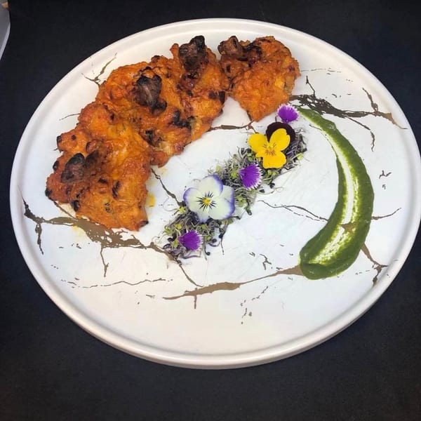 Indian pakoras with green sauce and edible flowers on a white and gold marbled plate.