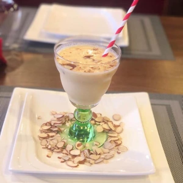 An Indian almond drink in a green-stemmed glass with a red and white straw, surrounded by almonds.