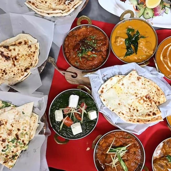 Overhead view of various Indian dishes including naan bread, curries, and palak paneer on a red tablecloth.