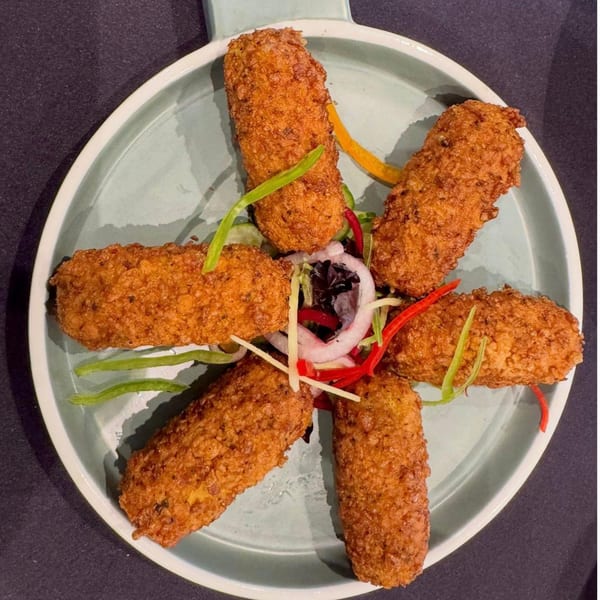Five golden-brown fried Indian croquettes arranged in a star shape on a light blue plate, garnished with colorful vegetables.