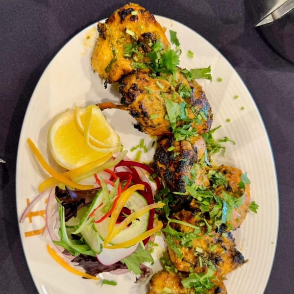 Grilled chicken tikka skewers, garnished with fresh cilantro, lemon, and a side salad.