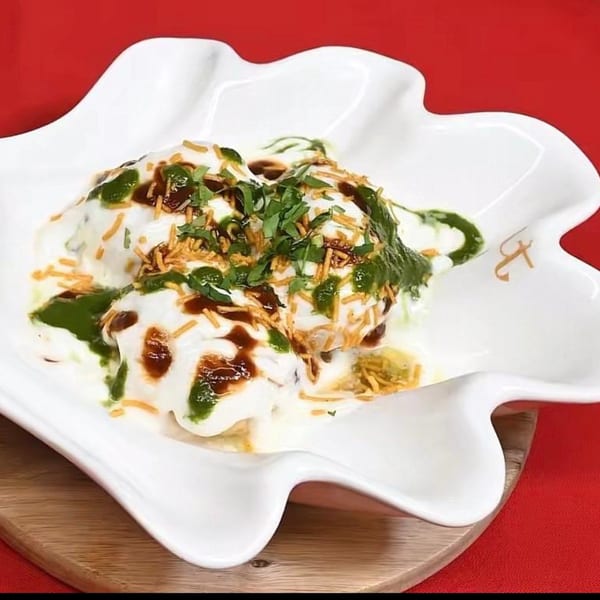 Dahi Bhalla, an Indian dish, topped with yogurt, green chutney, tamarind chutney, and sev in a white bowl.