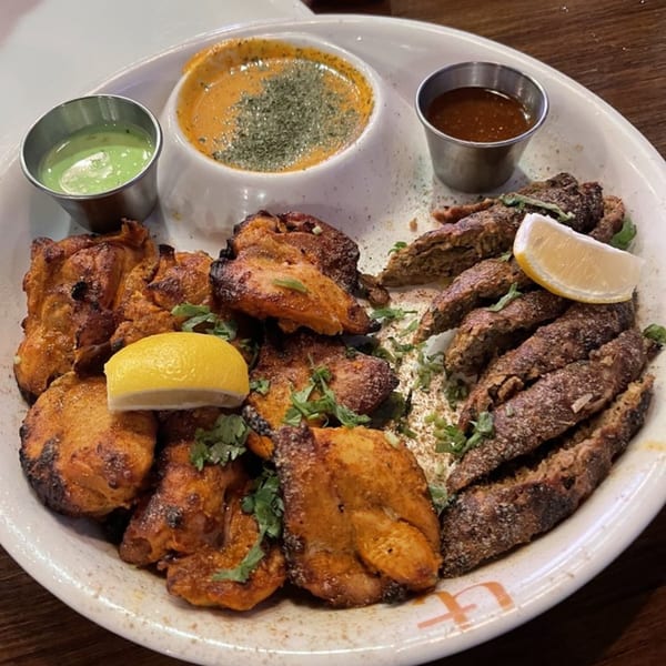Indian platter with tandoori chicken, seekh kebab, and three dipping sauces, garnished with lemon and cilantro.