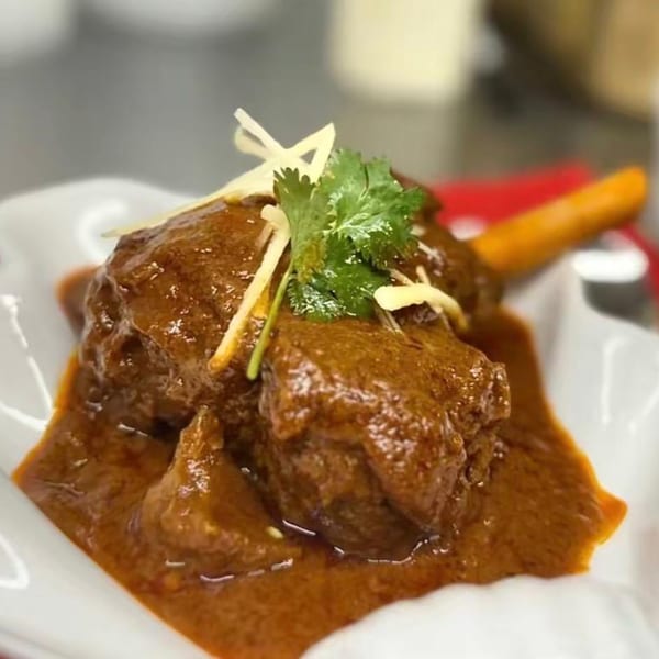 Rich brown Indian curry with meat, garnished with fresh cilantro and ginger slivers.