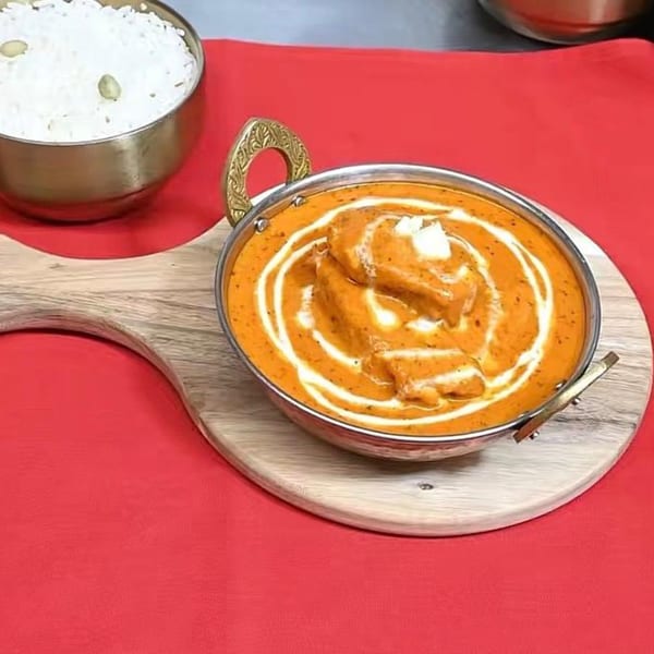 Indian butter chicken in a metal bowl with rice, served on a wooden board and red tablecloth.