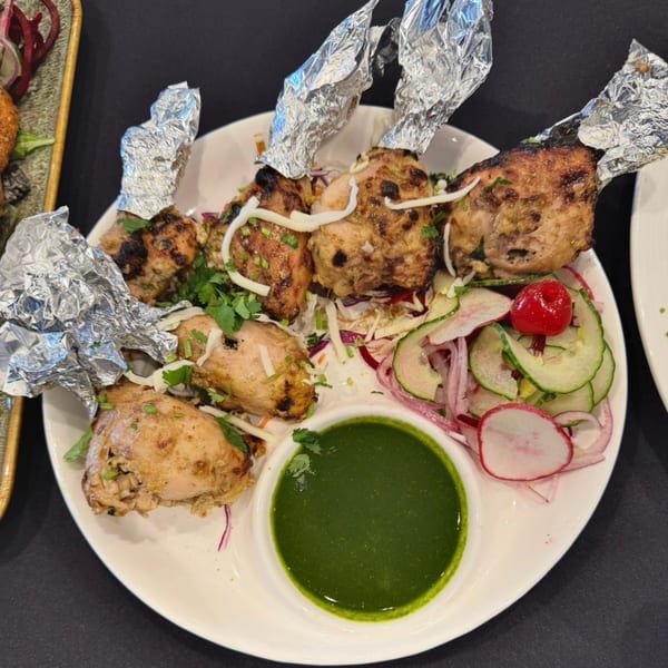 Indian chicken lollipops with foil-wrapped bones, green chutney, and a side salad with radishes.
