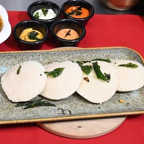 Four idlis garnished with curry leaves and spices, served with four small bowls of chutneys.