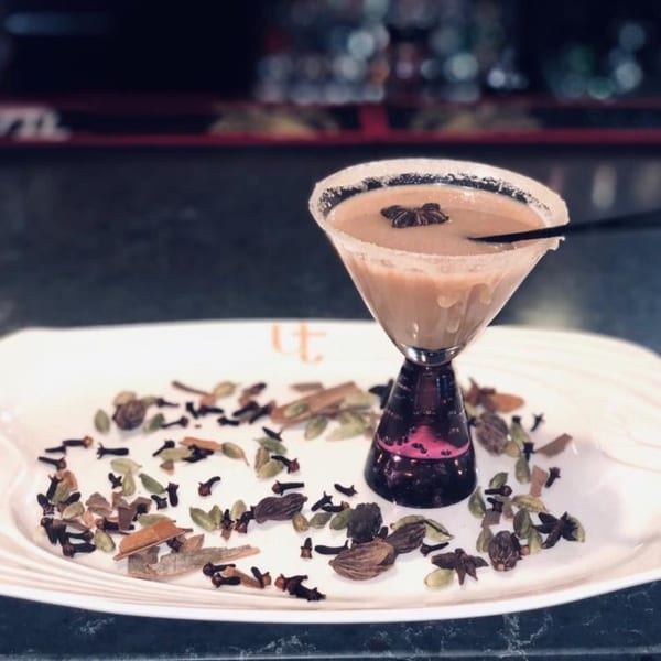 Chai martini with a star anise garnish, surrounded by cloves, cardamom, and cinnamon sticks.