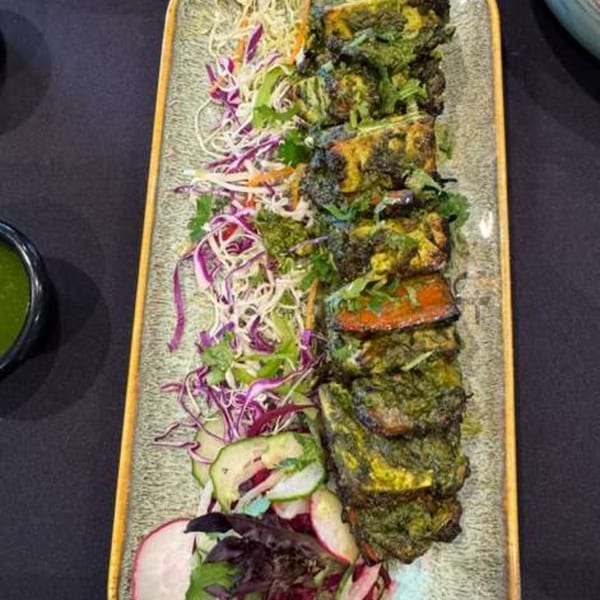Indian paneer tikka with green marinade, served with shredded cabbage, cucumber, and radish salad.