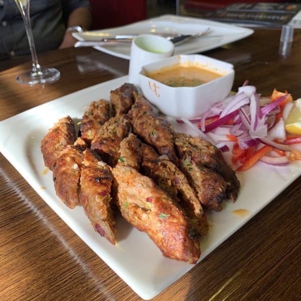 Indian seekh kebabs with dipping sauce and a side of red onion salad on a white plate.