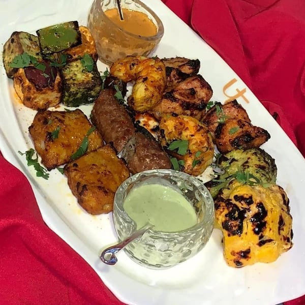 A white platter of Indian tandoori chicken, paneer, and vegetables with two dipping sauces.