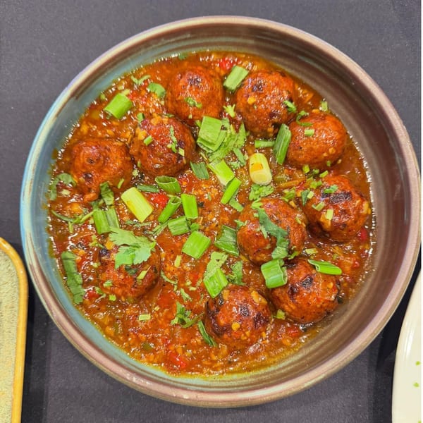 A bowl of Urban Tandoor's Indian meatballs in a rich red sauce, garnished with fresh herbs.