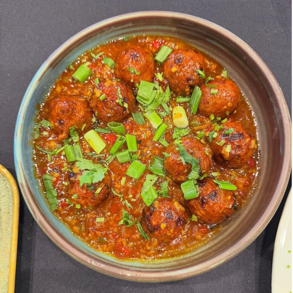 A bowl of Urban Tandoor's Indian meatballs in a rich red sauce, garnished with fresh herbs.