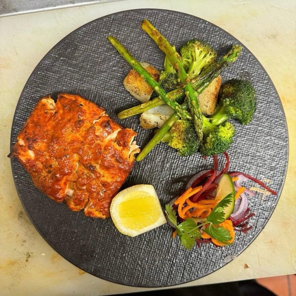 Indian-spiced fish with roasted asparagus, broccoli, and a side salad with lemon on a dark plate.
