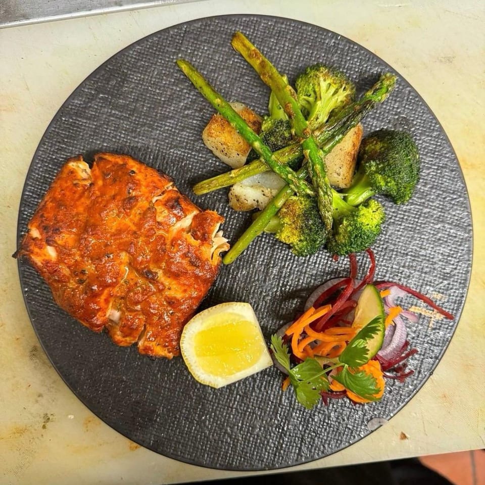 Indian-spiced fish with roasted asparagus, broccoli, and a side salad with lemon on a dark plate.