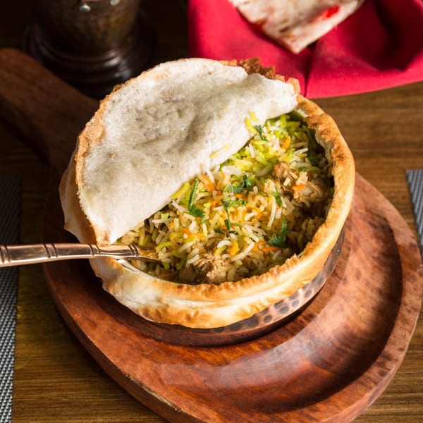 Urban Tandoor's chicken biryani, a colorful rice dish with herbs, served in a bread-covered pot.
