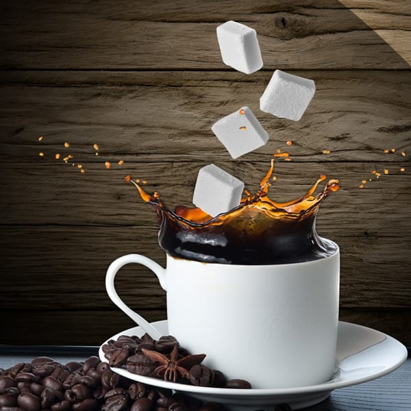 Sugar cubes splashing into a cup of coffee, with coffee beans and star anise on the saucer.