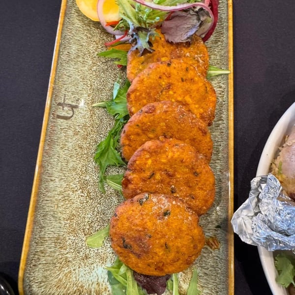 Six golden-brown Indian lentil fritters, garnished with fresh greens and red onion, on a rectangular plate.