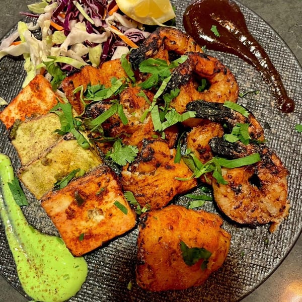 A platter of grilled Indian paneer, chicken, and shrimp with coleslaw, green chutney, and tamarind sauce.