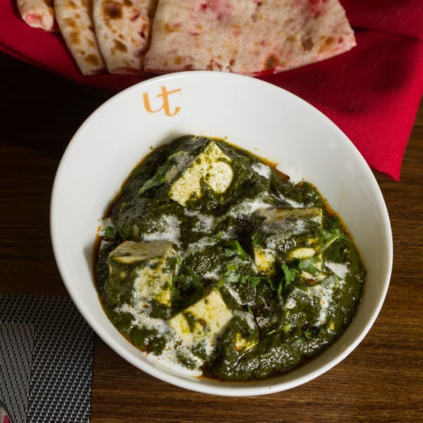 A white bowl of Urban Tandoor's Palak Paneer, a creamy green spinach dish with paneer cheese cubes.
