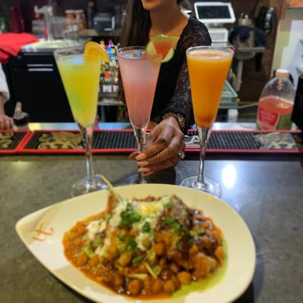 A plate of Indian chana masala with three colorful cocktails on a bar counter at Urban Tandoor.