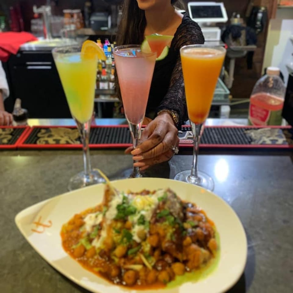 A plate of Indian chana masala with three colorful cocktails on a bar counter at Urban Tandoor.