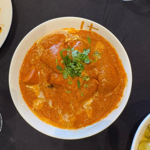 A bowl of Urban Tandoor's Indian butter chicken, garnished with fresh cilantro, on a dark table.